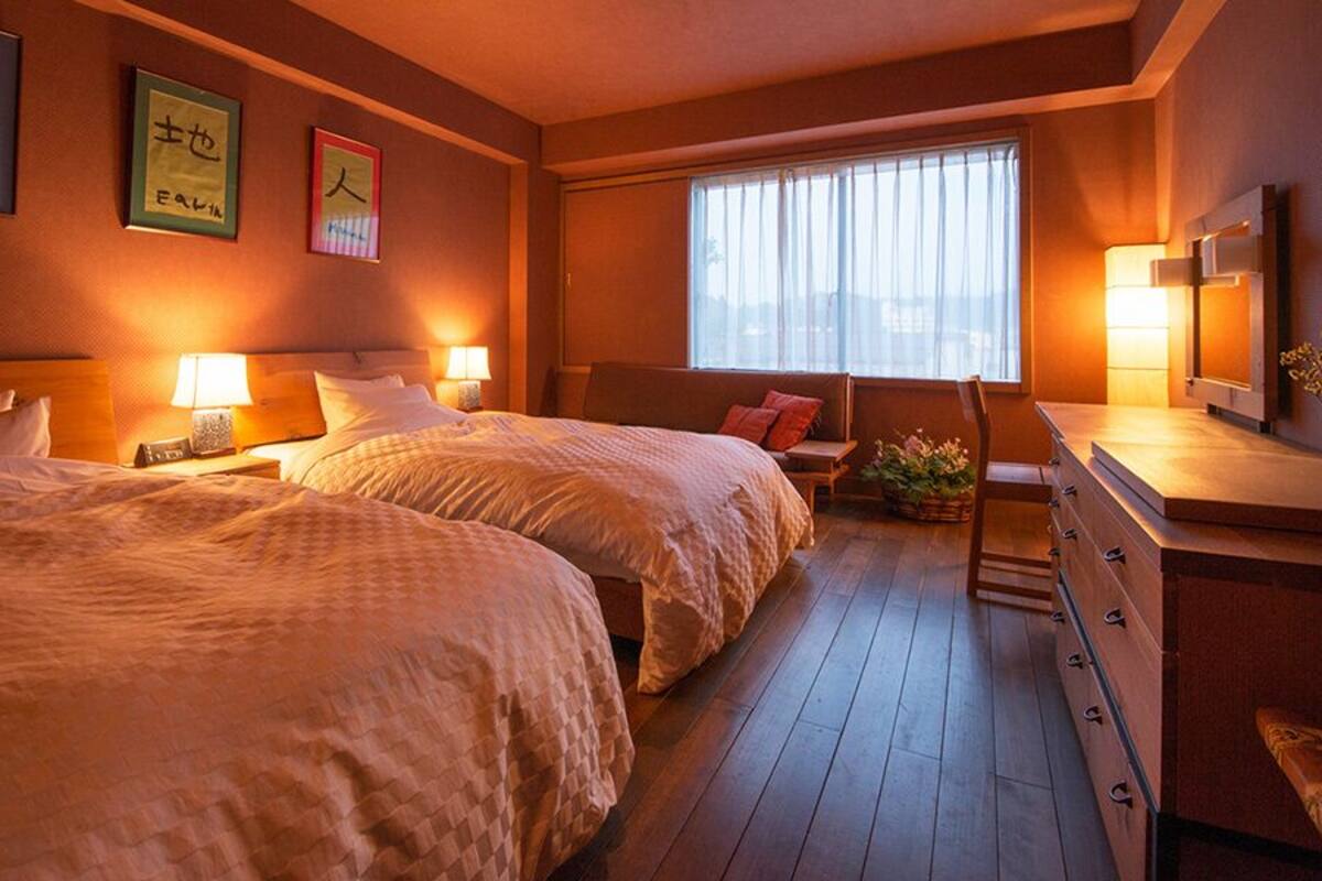 Una habitación de hotel con dos camas, lámparas de noche, un escritorio con una silla y una ventana con cortinas.