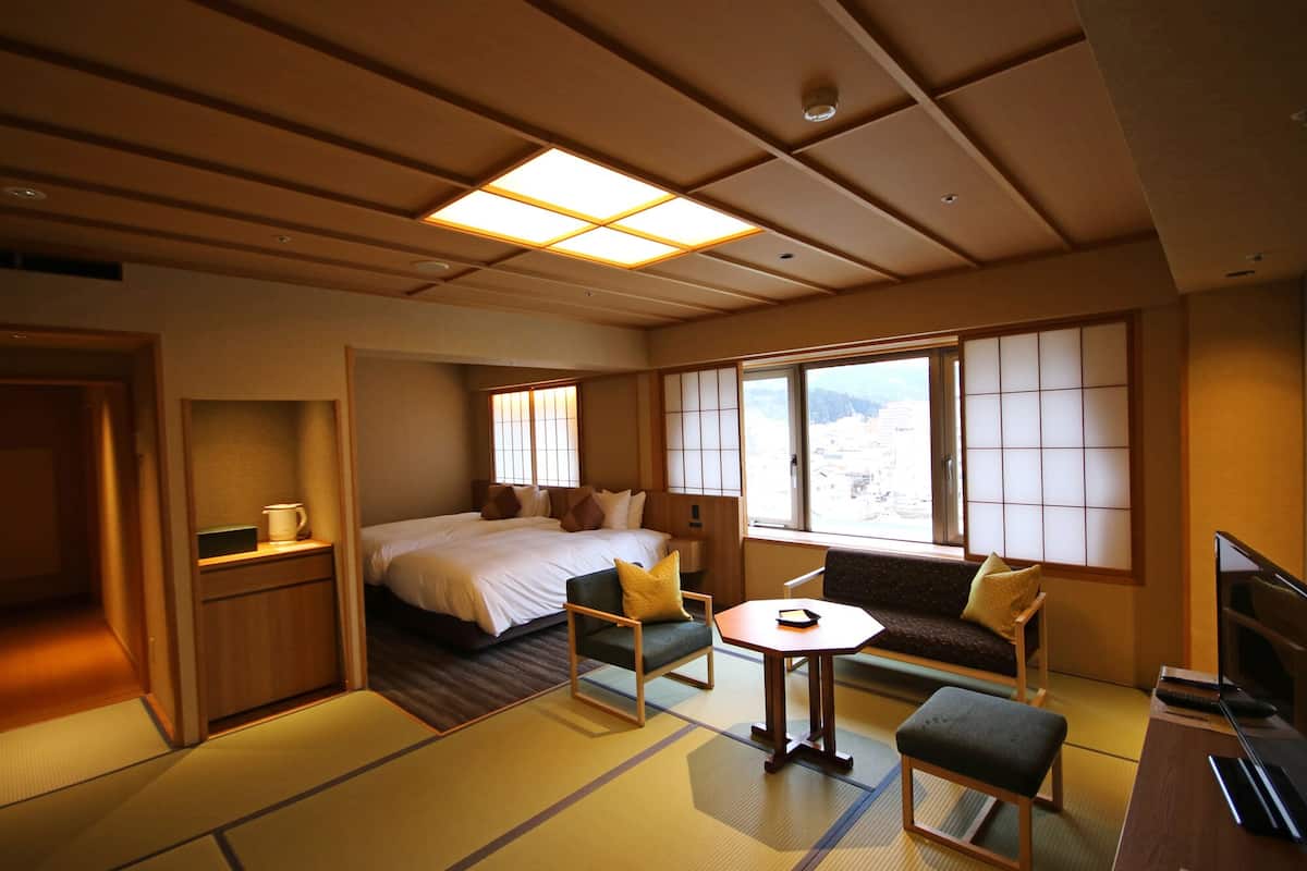 Una habitación tradicional japonesa con suelo de tatami, una cama, un sofá, una mesita y un televisor.