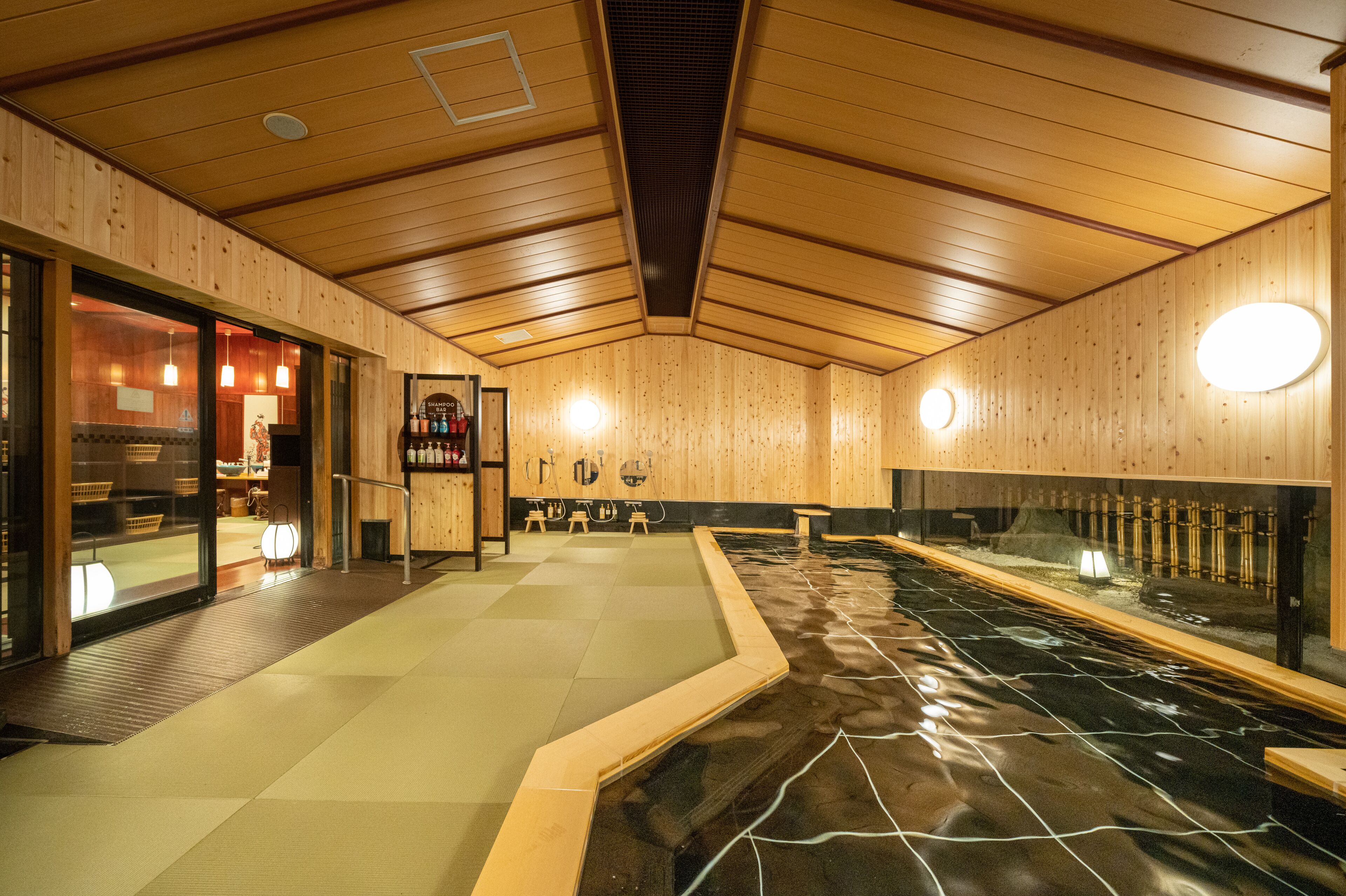 A traditional wooden interior with a hot spring bath, wooden walls, and a reception area with a counter and chairs.