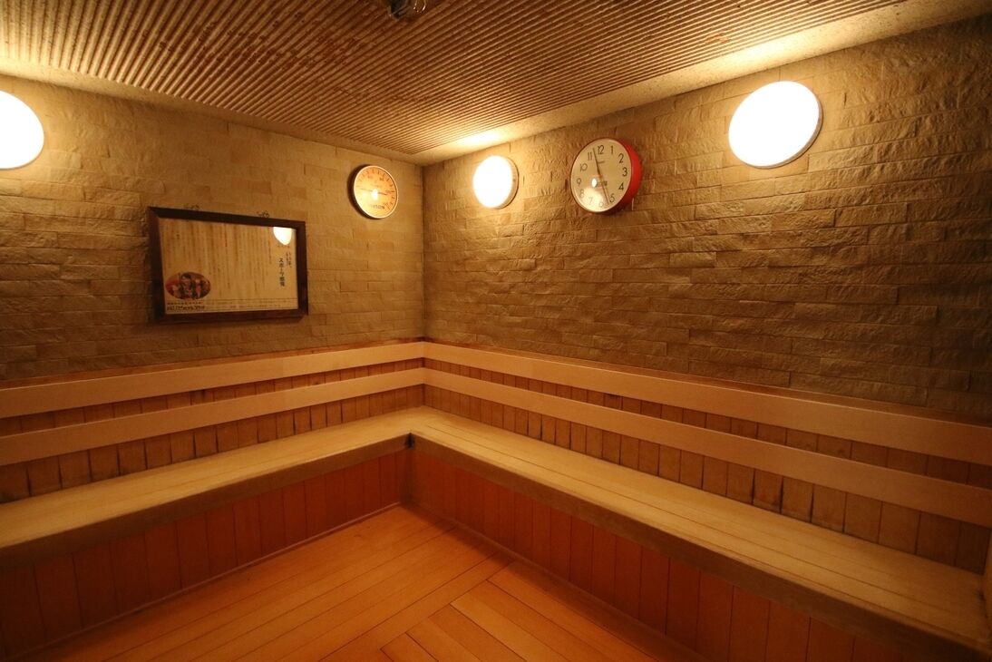 A sauna room with wooden benches, a brick wall, and three wall-mounted clocks.