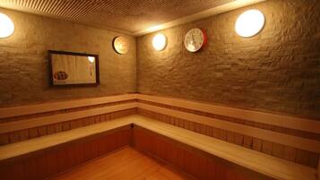 A sauna room with wooden benches, a brick wall, and three wall-mounted clocks.