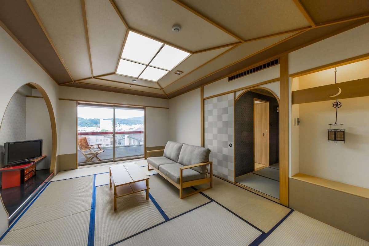 Una habitación con suelo de tatami, un sofá, un televisor, un balcón con vistas y un ventanal corredero.