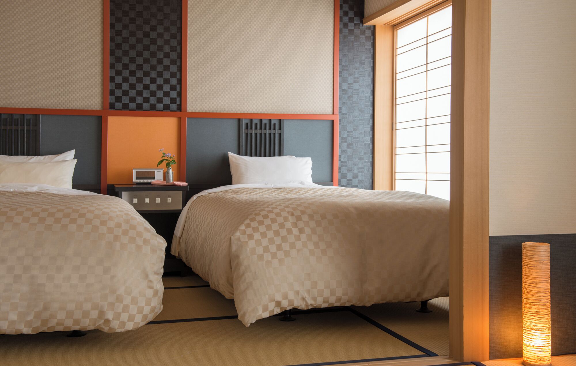 A hotel room with two beds, a bedside table with a radio, and a traditional Japanese-style window.