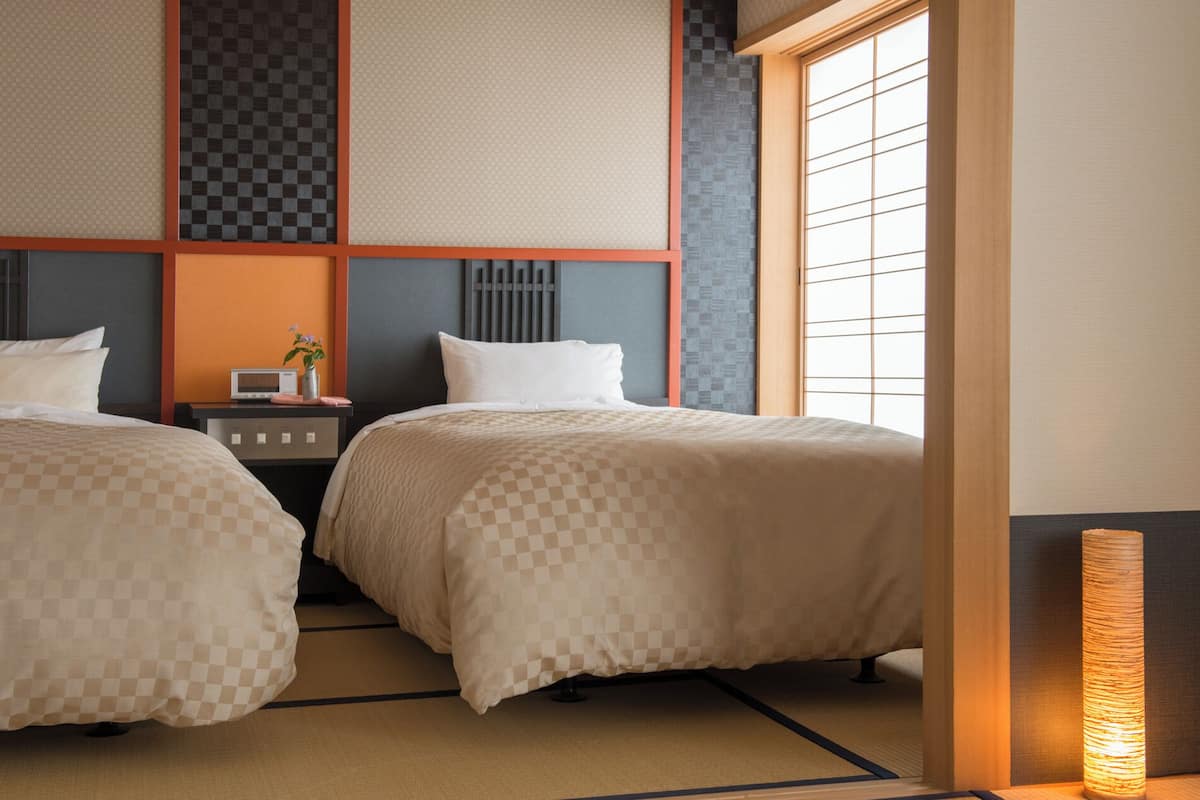 Habitación de hotel con dos camas, una mesita de noche con radio y una ventana de estilo tradicional japonés.