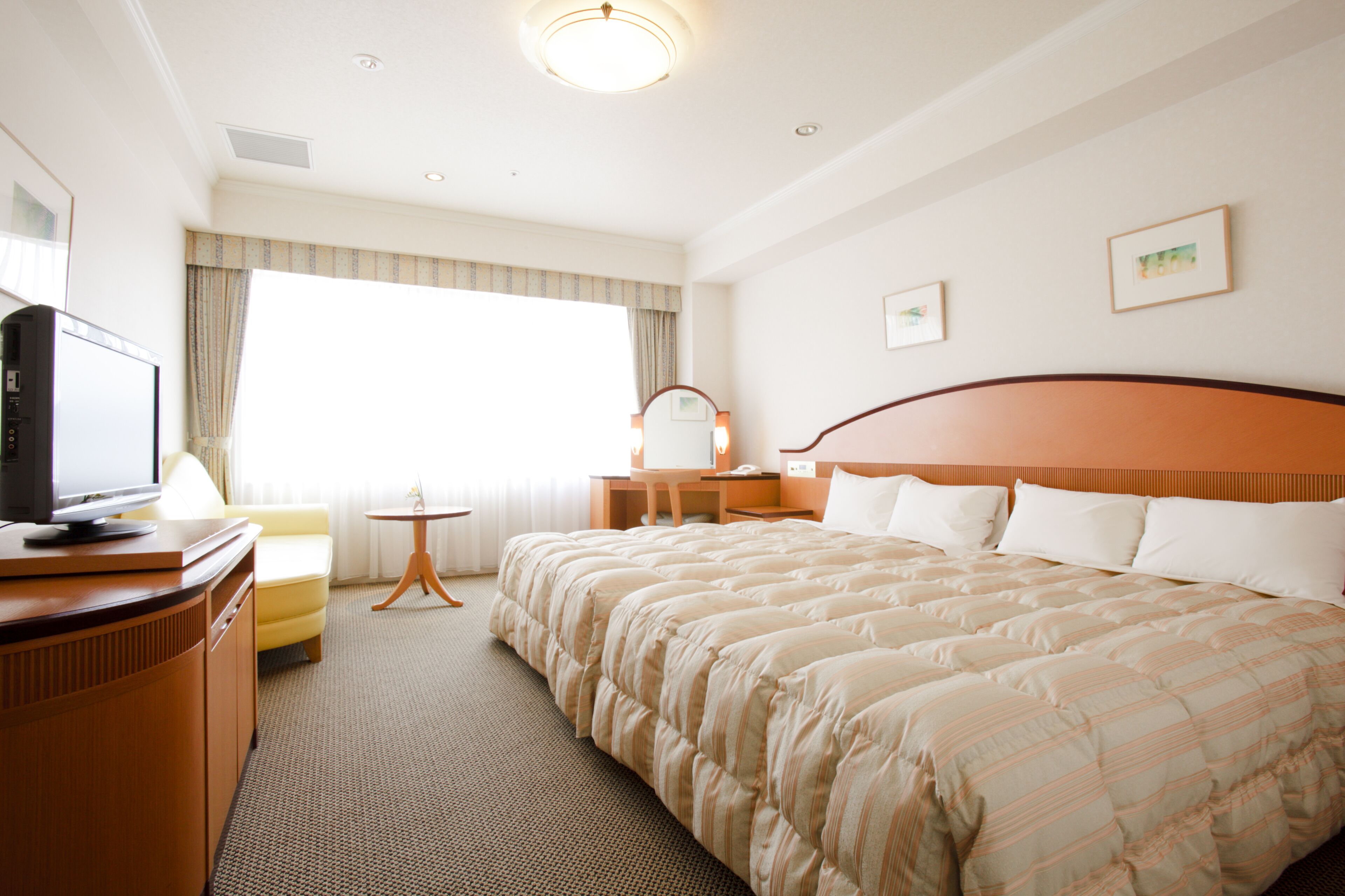 A hotel room with a large bed, a desk with a chair, a television, and a small table.