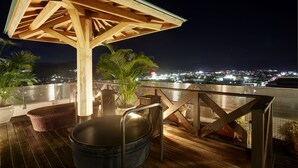 A wooden deck with a hot tub, potted plants, and a view of a cityscape at night. - Hida Hotel Plaza (Takayama)