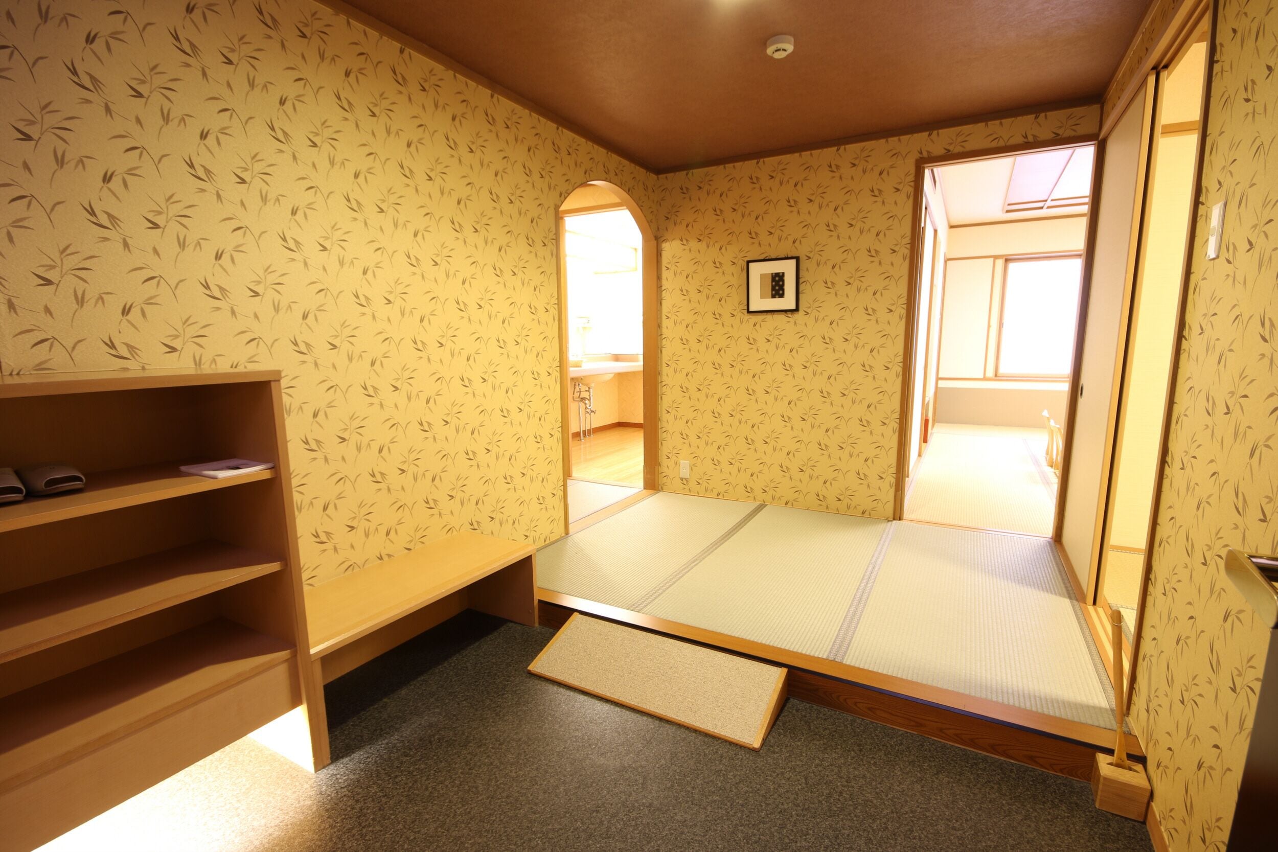 A room with tatami flooring, a low wooden bed, a shelf with books, and a window with a view.