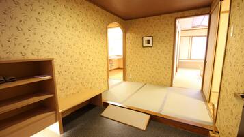 A room with tatami flooring, a low wooden bed, a shelf with books, and a window with a view.