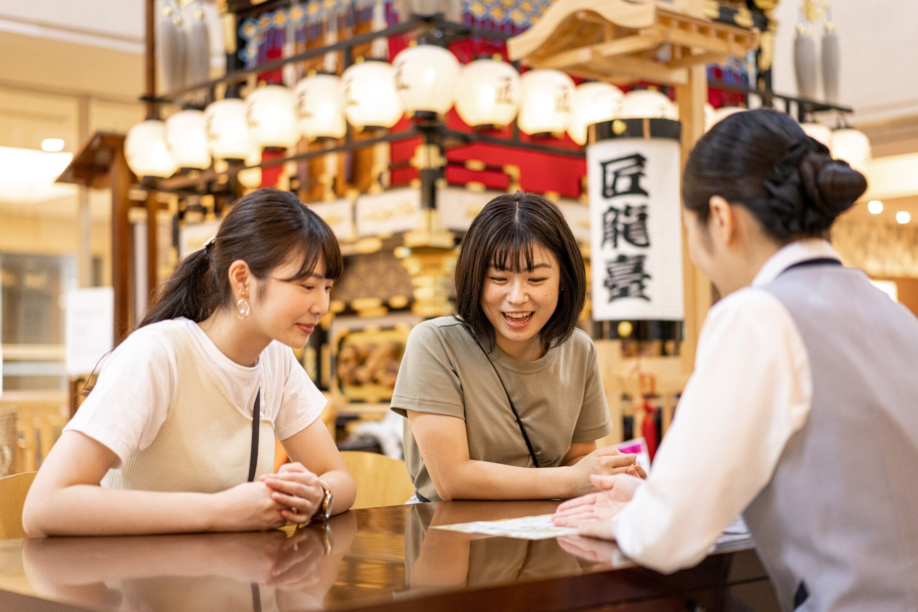 Trois personnes sont assises à une table dans un restaurant à la décoration traditionnelle, avec des lanternes en arrière-plan.