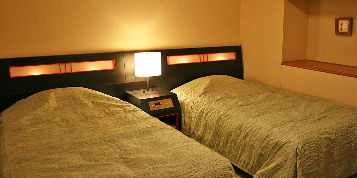 A hotel room with two single beds, a nightstand with a lamp, and a small table.