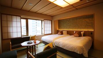 Quarto de hotel com uma cama grande, uma mesinha, um sofá e vista para edifícios pela janela.