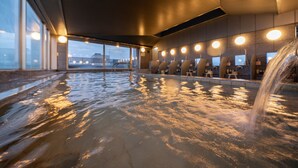 A large indoor swimming pool with a waterfall feature, surrounded by seating areas and large windows. - Hida Hotel Plaza (Takayama)