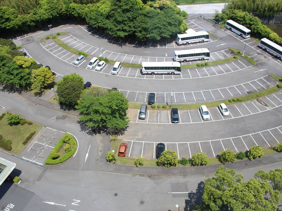 Luchtbeeld van een parkeerplaats met meerdere parkeerplaatsen, enkele auto's en verschillende bussen.