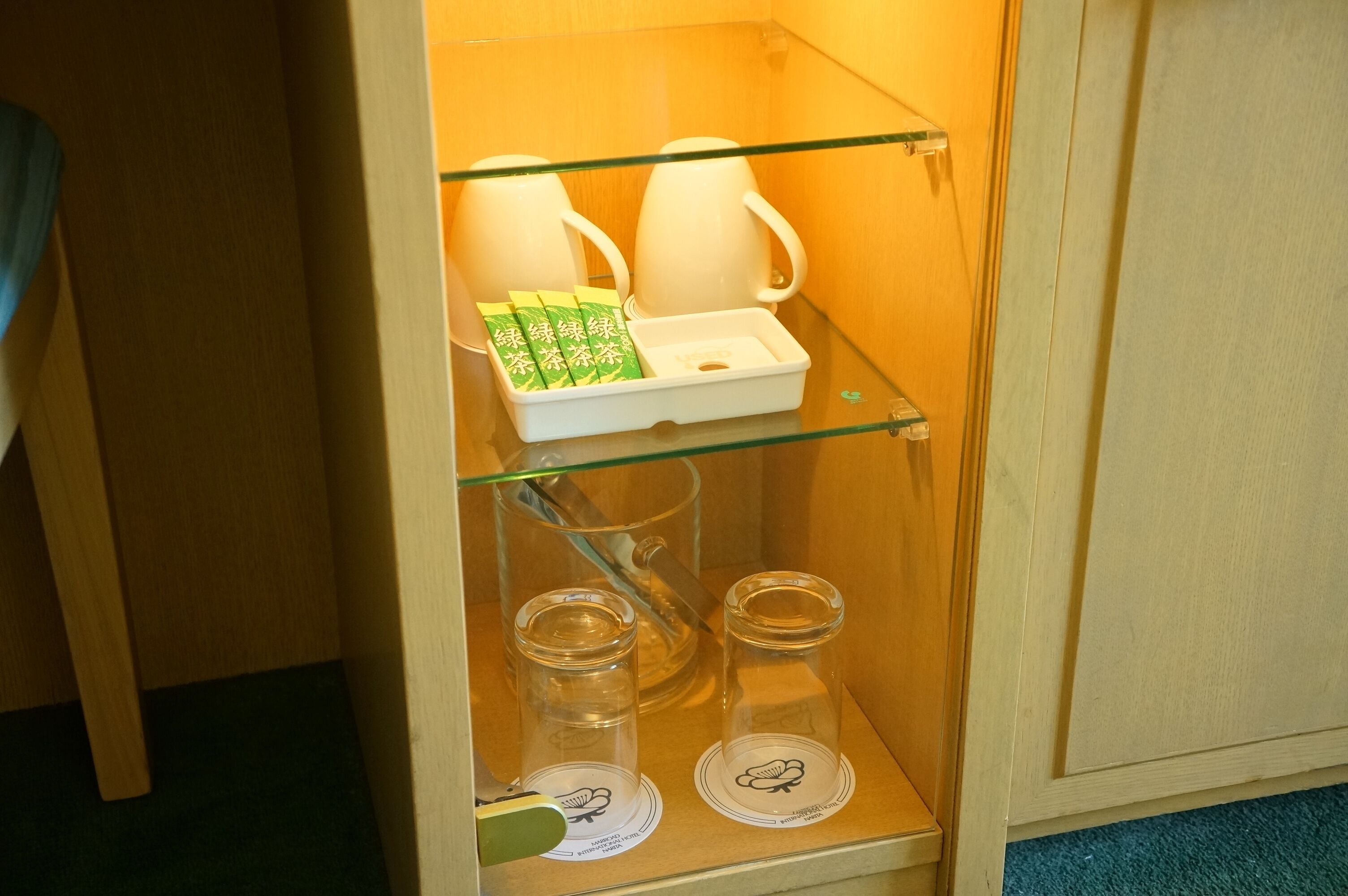 Un mueble con puerta de vidrio que contiene un juego de té y bolsitas de té.