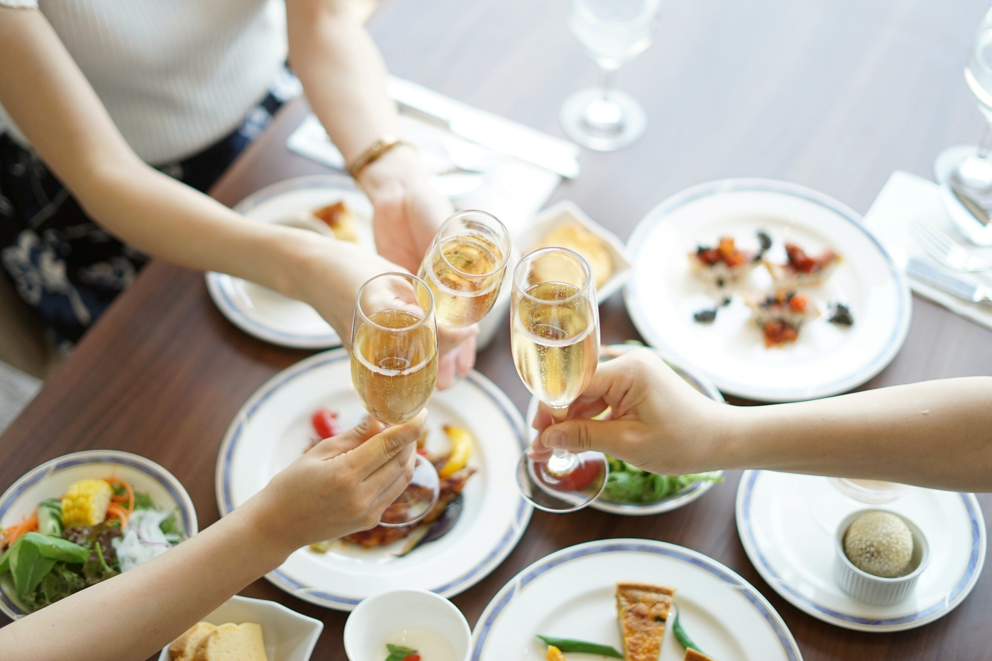 Un groupe de personnes trinquant avec des coupes de champagne autour d’une table à dîner où sont servis différents plats.