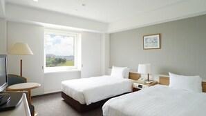 A hotel room with two beds, a desk, a chair, a TV, a window with a view, and a painting on the wall.