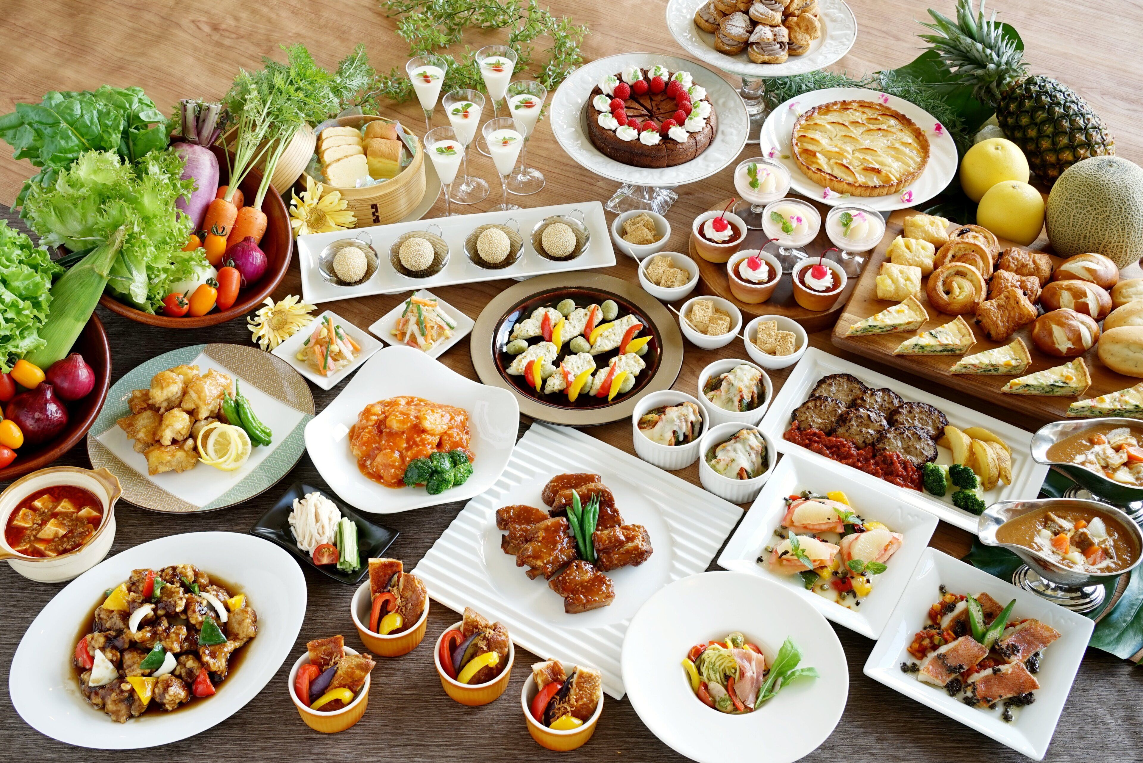 Diversos pratos e alimentos sobre uma mesa, incluindo saladas, carnes e sobremesas.