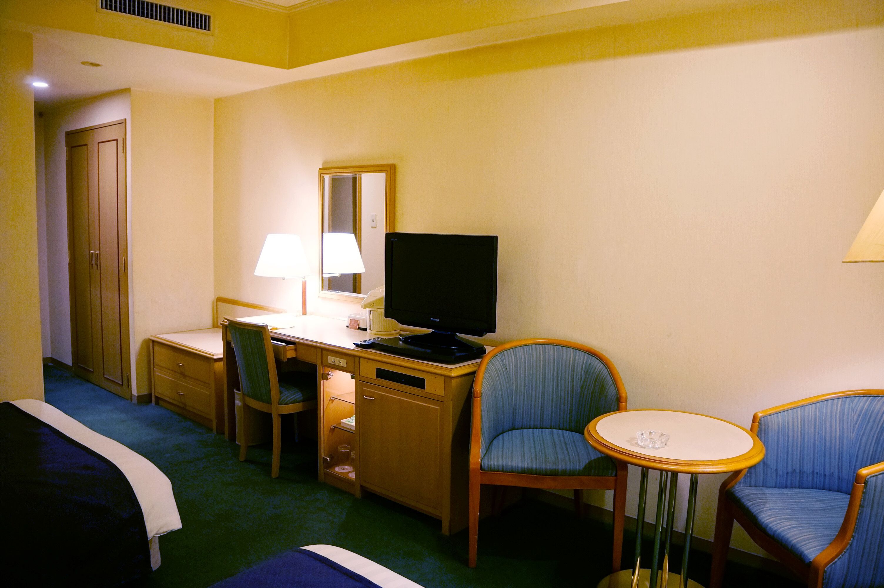 Una habitación de hotel con cama, escritorio, silla, televisor y una pequeña mesa.