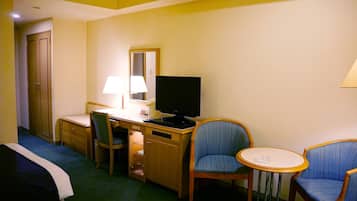Una habitación de hotel con cama, escritorio, silla, televisor y una pequeña mesa.