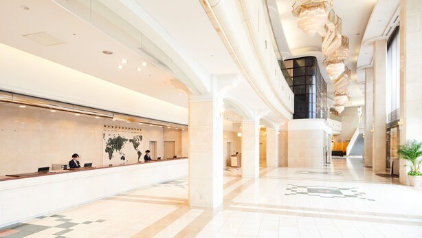 A spacious lobby with a reception desk, a large chandelier, and a high ceiling.