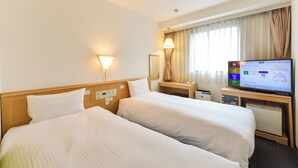 A hotel room with two beds, a desk with a computer, and a window with curtains.