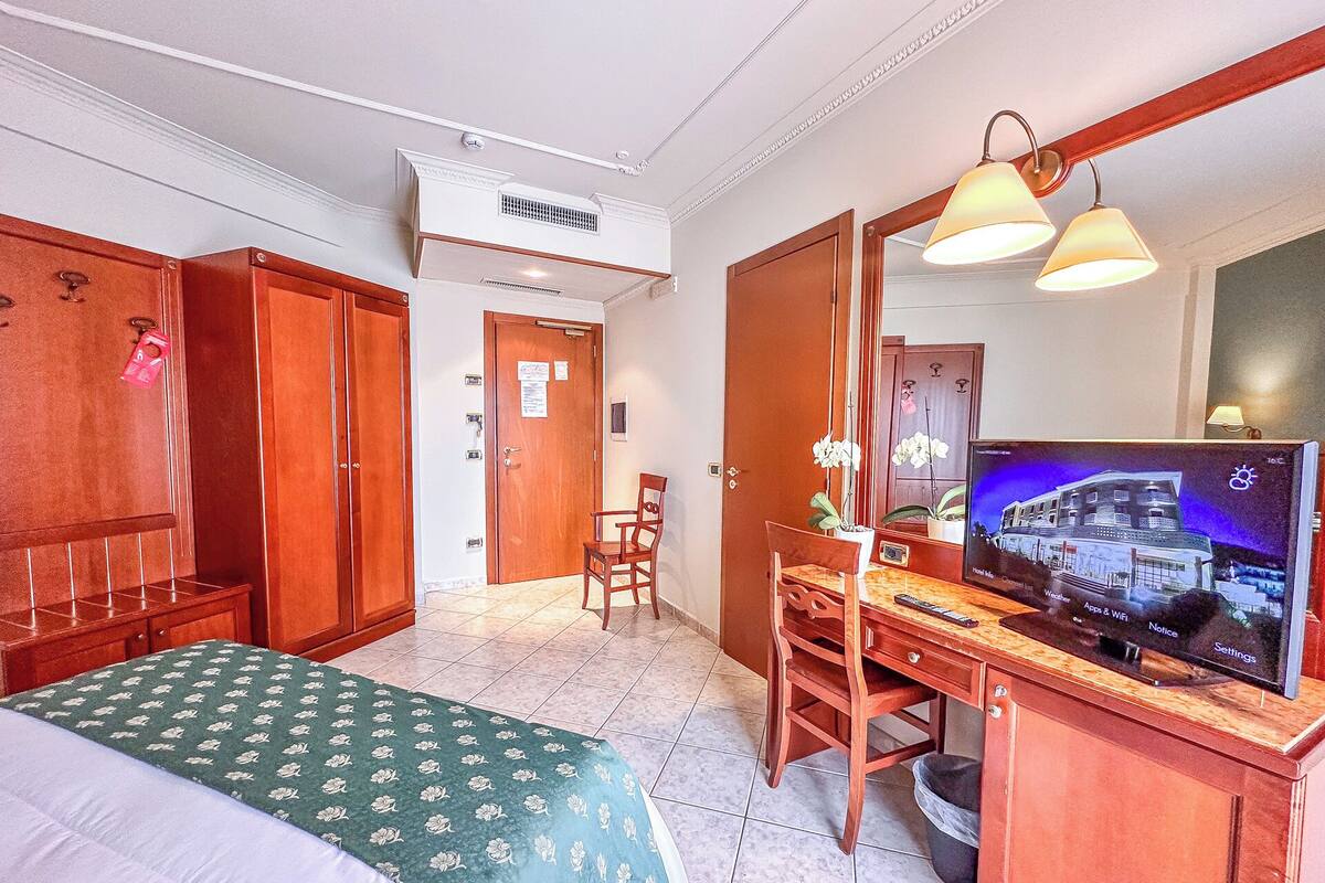 A hotel room with a bed, a desk with a TV, a chair, and a wardrobe.