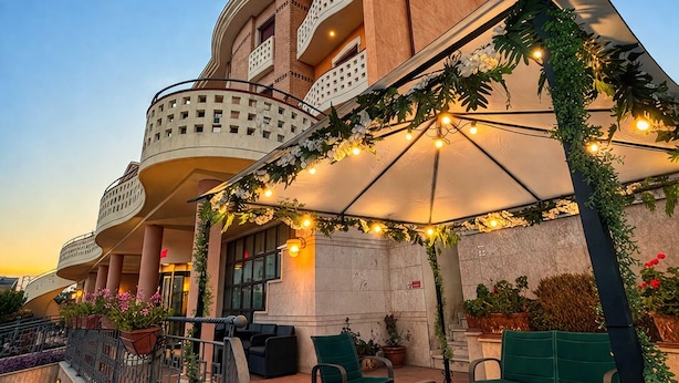 Een hotel met een gebogen gevel, terras en decoratieve verlichting.