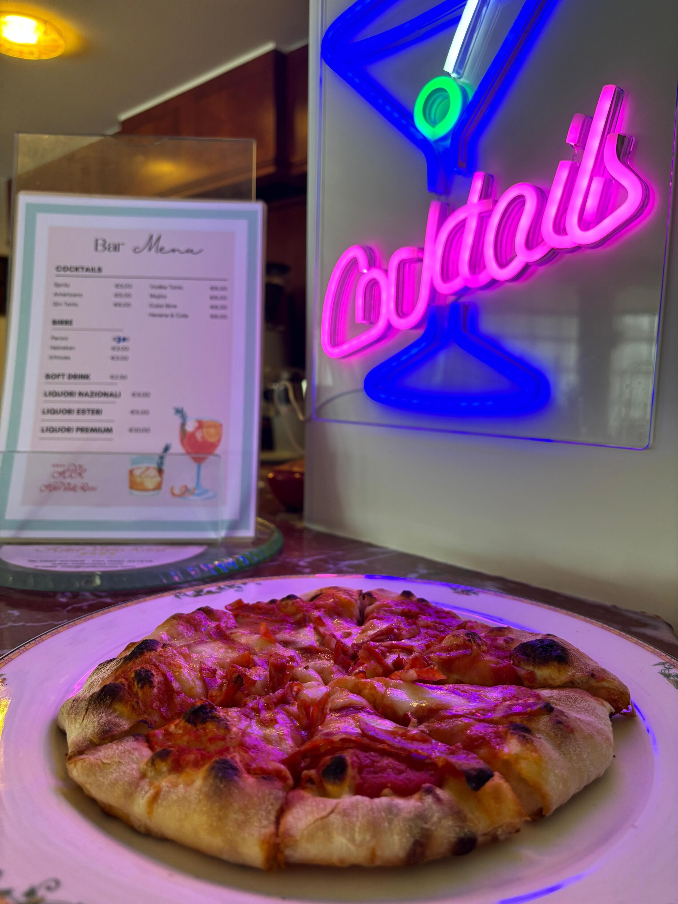 A pizza on a plate with a neon sign in the background.