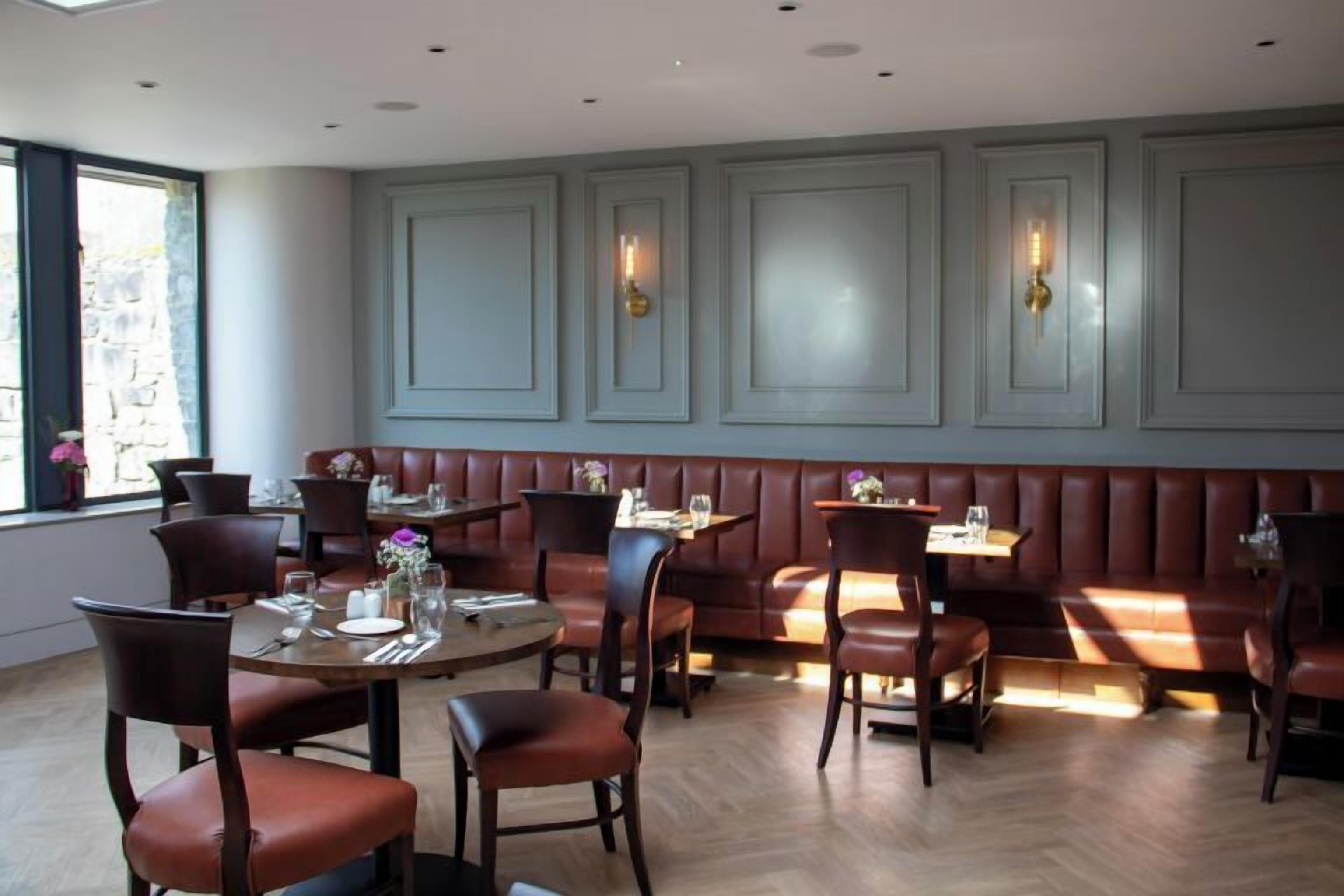 A restaurant with round tables and booths, wooden flooring, and light-colored walls with decorative wall sconces.
