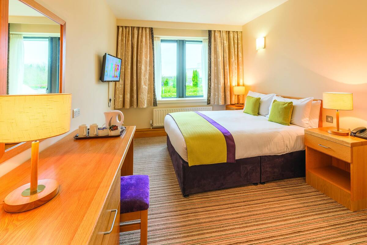 A hotel room with a bed, a desk, a chair, a television, and a window with curtains.