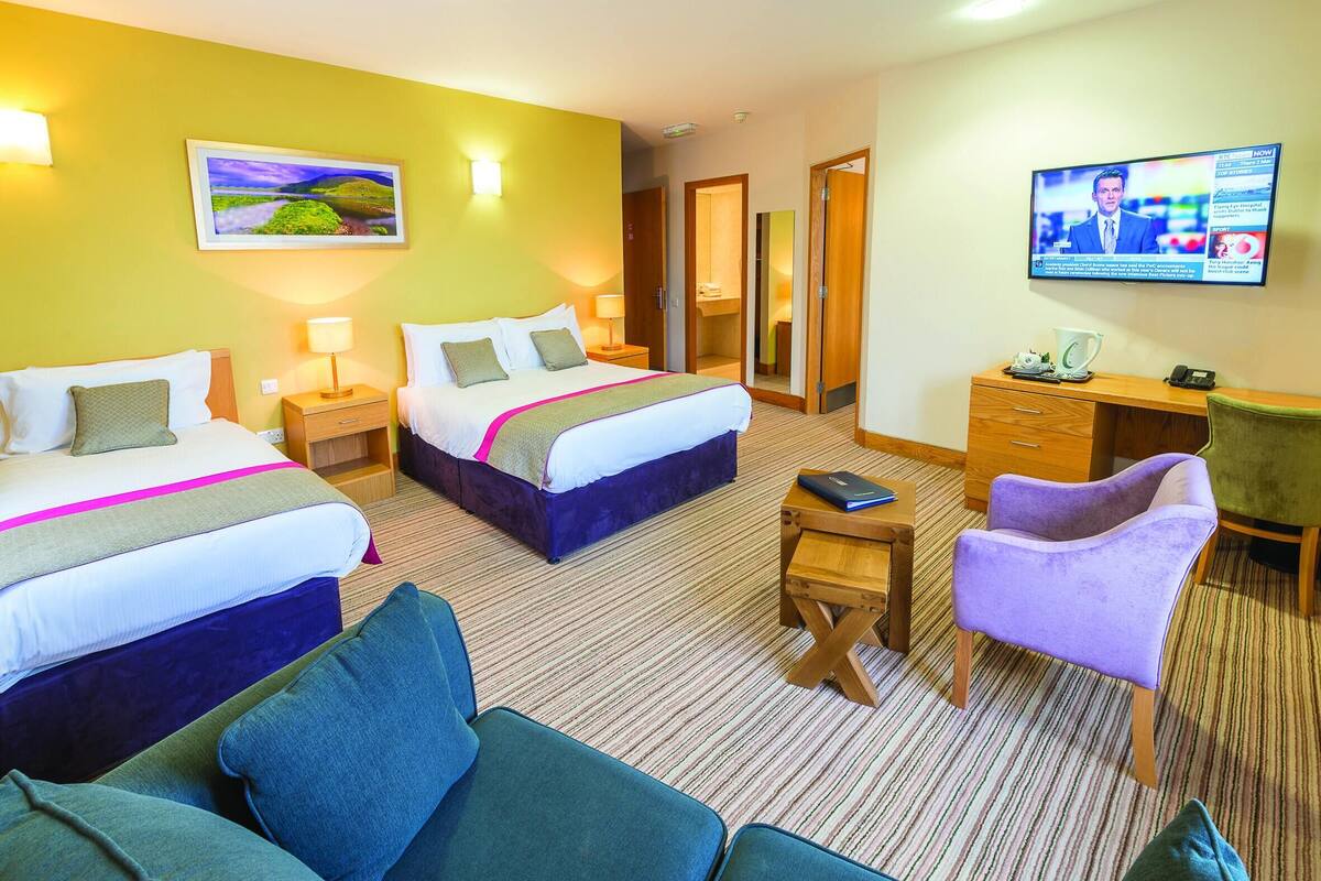 A hotel room with two beds, a desk, a chair, a television, and a painting on the wall.