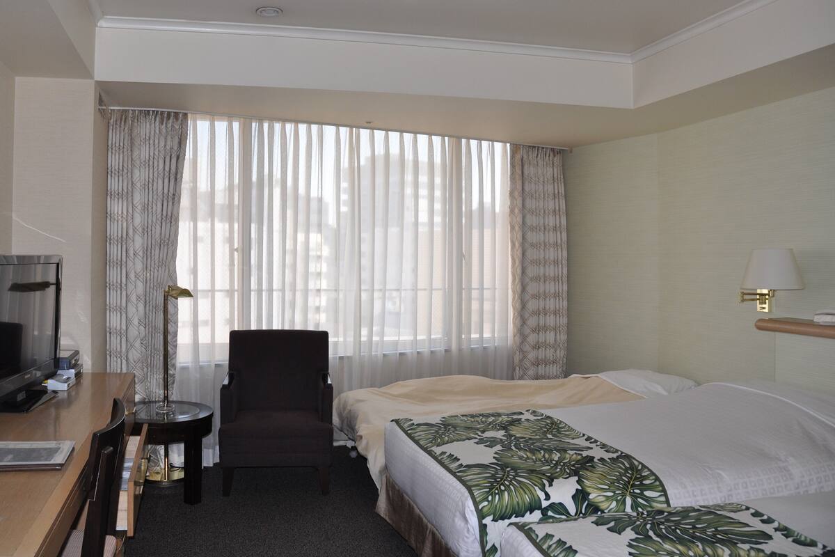 Une chambre d’hôtel avec un lit, une chaise, un bureau avec une télévision et une lampe.