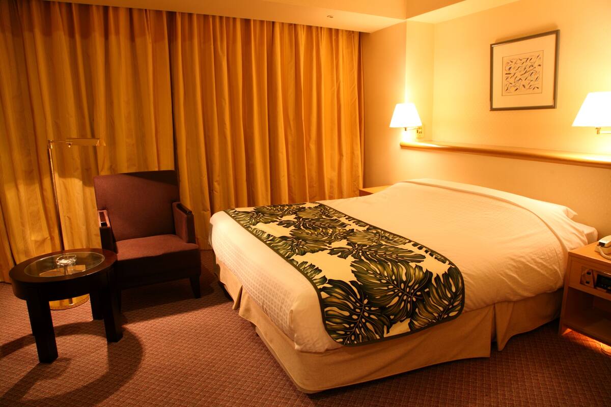 Une chambre d’hôtel avec un lit, une chaise, une petite table et une table de chevet avec une lampe.
