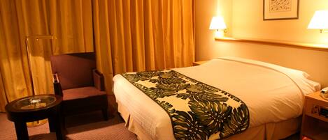 A hotel room with a bed, a chair, a small table, and a nightstand with a lamp.