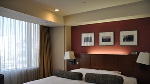 Ein Hotelzimmer mit einem großen Bett, zwei Nachttischlampen, einem Nachttisch und einem Fenster mit transparenten Vorhängen.