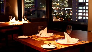 Ein gedeckter Restauranttisch mit Tellern, Besteck und Gläsern, mit Blick auf eine Stadtlandschaft durch das Fenster.