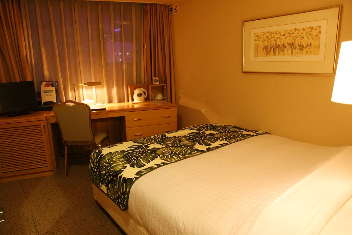 Une chambre d’hôtel comprenant un lit, un bureau avec une chaise, une télévision et une œuvre d’art encadrée accrochée au mur.