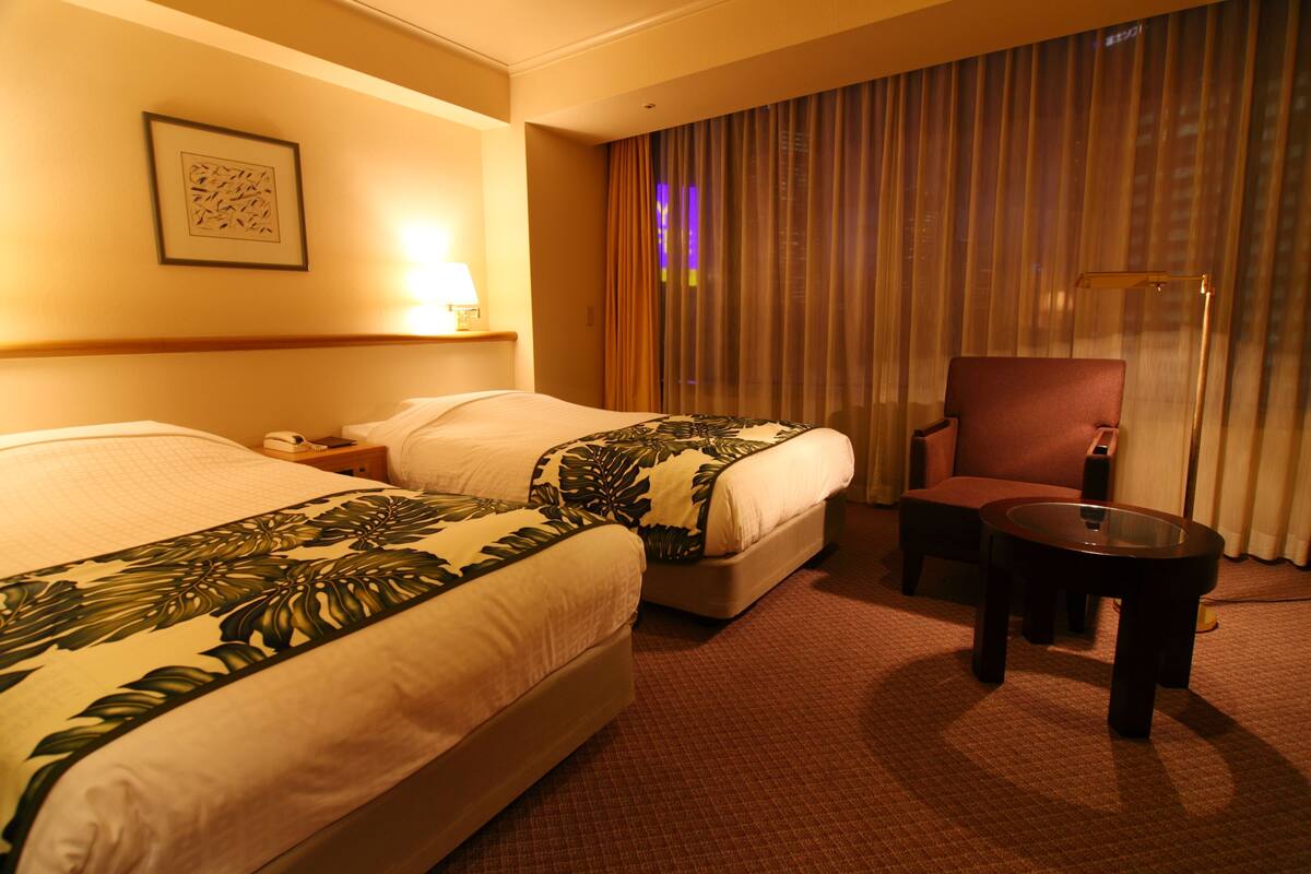 Une chambre d’hôtel avec deux lits, une chaise, une table et une lampe.