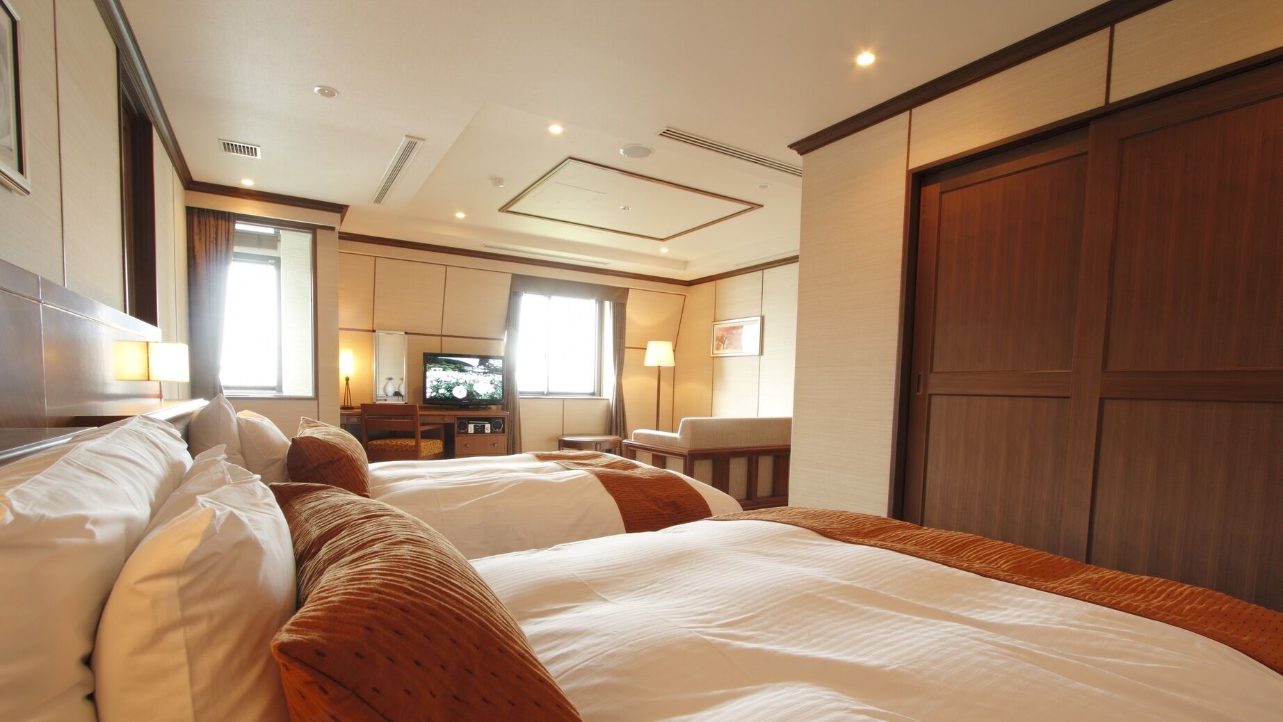 A hotel room with two beds, a television, a desk, and a wardrobe.