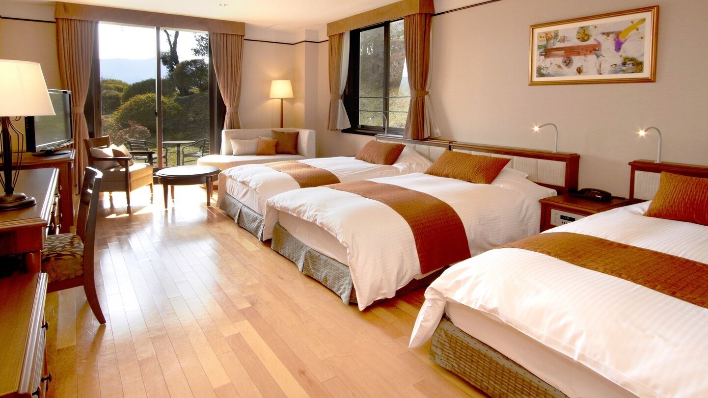 A hotel room with three beds, a TV, a desk, and a chair.