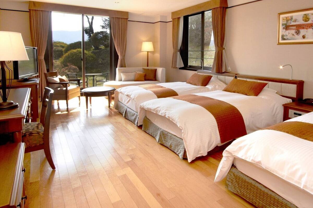 A hotel room with three beds, a TV, a desk, and a chair.