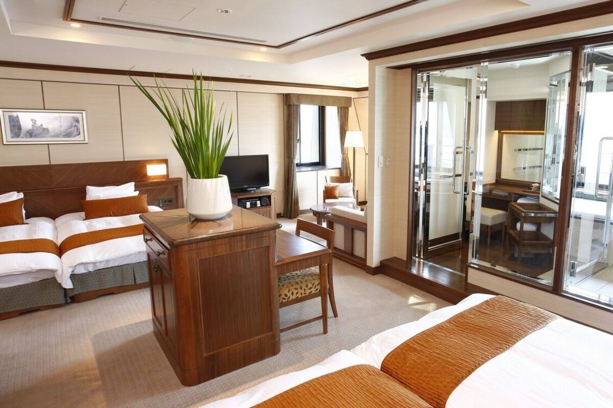 A hotel room with a bed, a desk, a television, a plant, and a sliding glass door to a balcony.