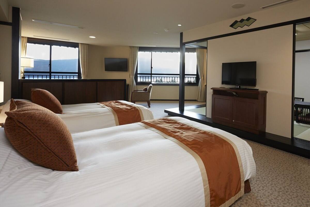A hotel room with two beds, a TV, a balcony, and a view of the mountains.