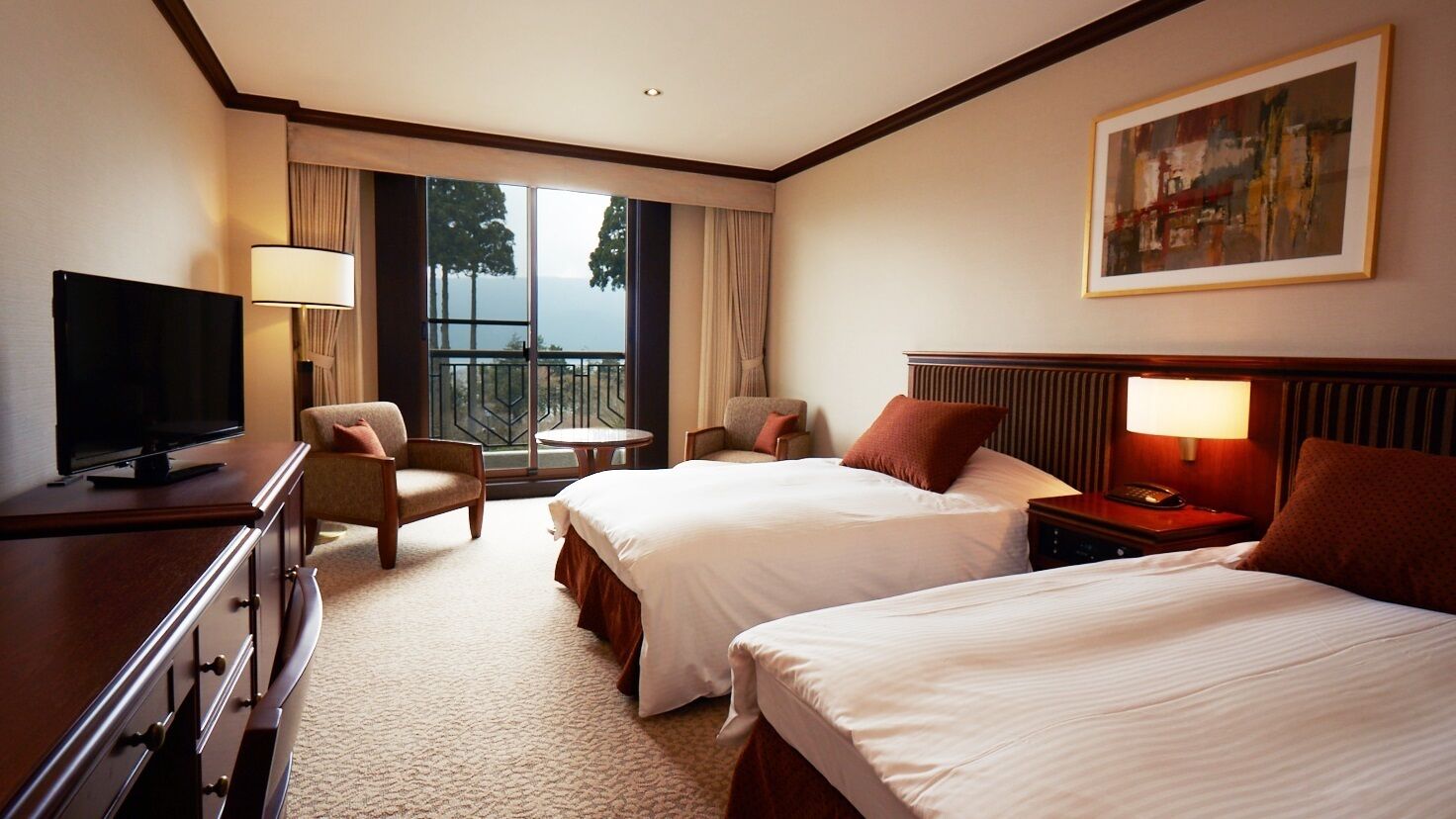 A hotel room with two beds, a TV, a desk, a chair, a lamp, and a painting on the wall.