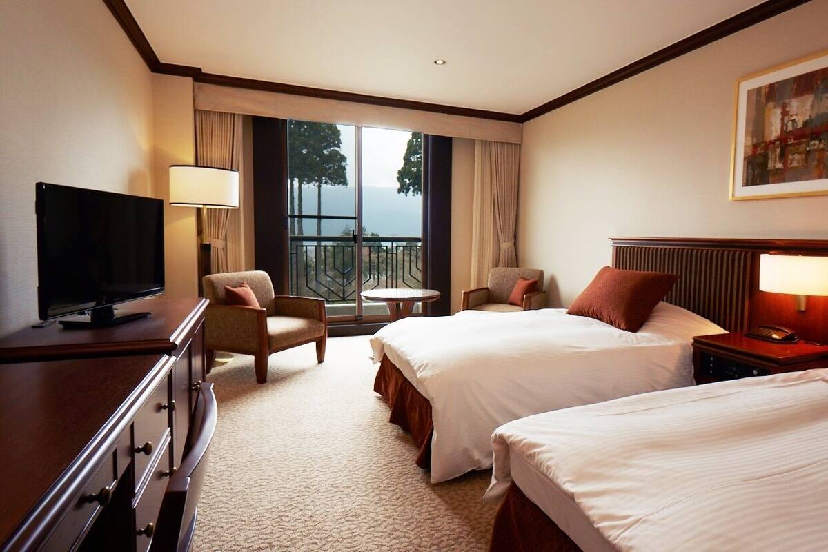 A hotel room with two beds, a TV, a desk, a chair, a lamp, and a painting on the wall.