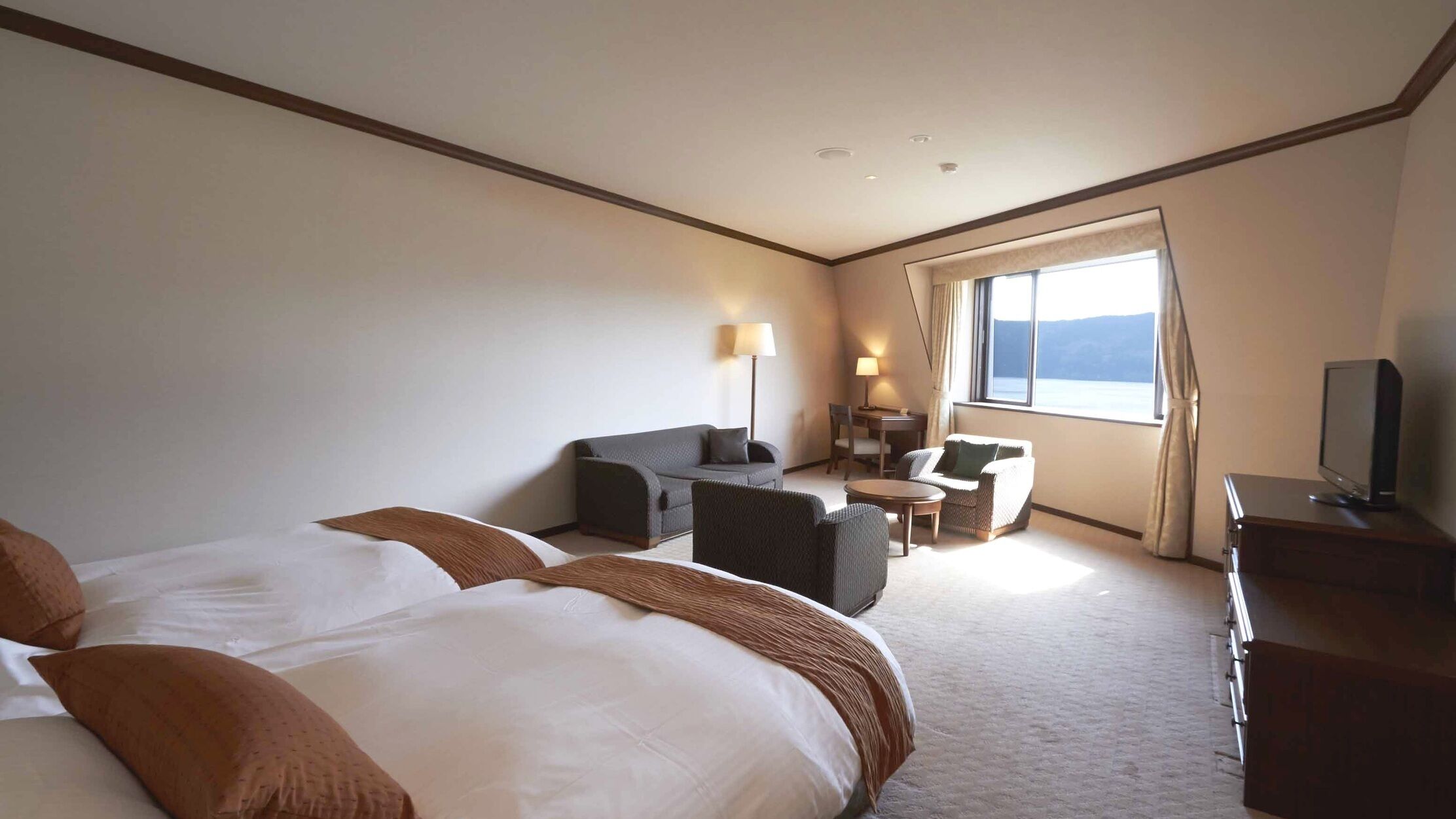 A hotel room with a large bed, a desk with a chair, a sofa, a TV, and a window with a view.