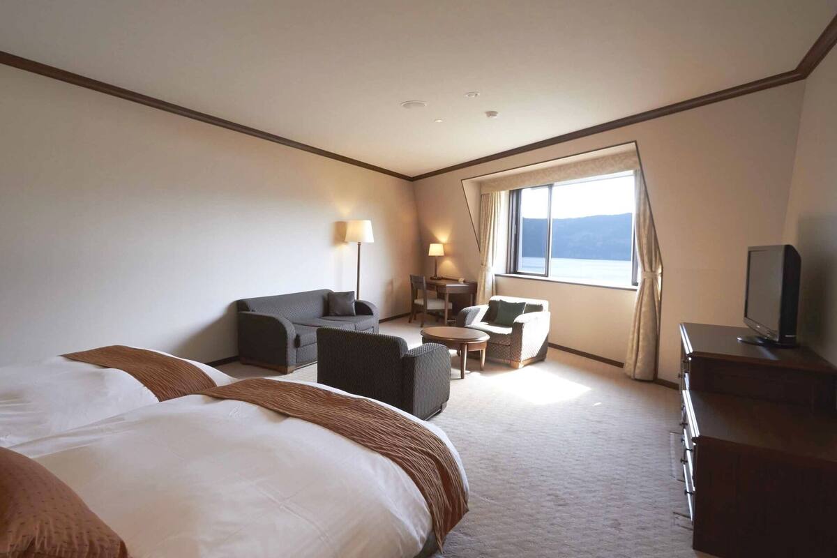 A hotel room with a large bed, a desk with a chair, a sofa, a TV, and a window with a view.