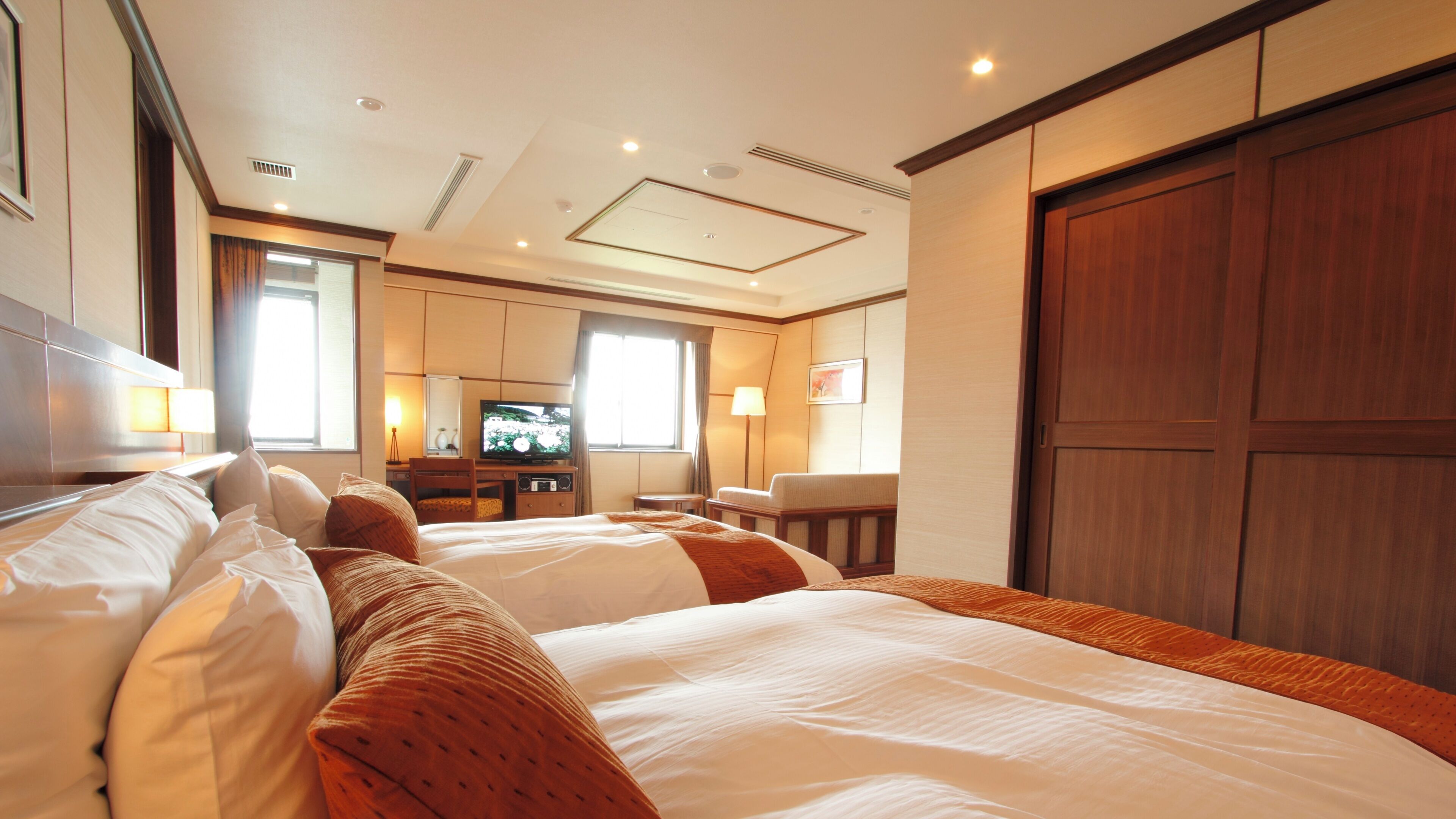 A hotel room with two beds, a television, a desk, and a large wardrobe.