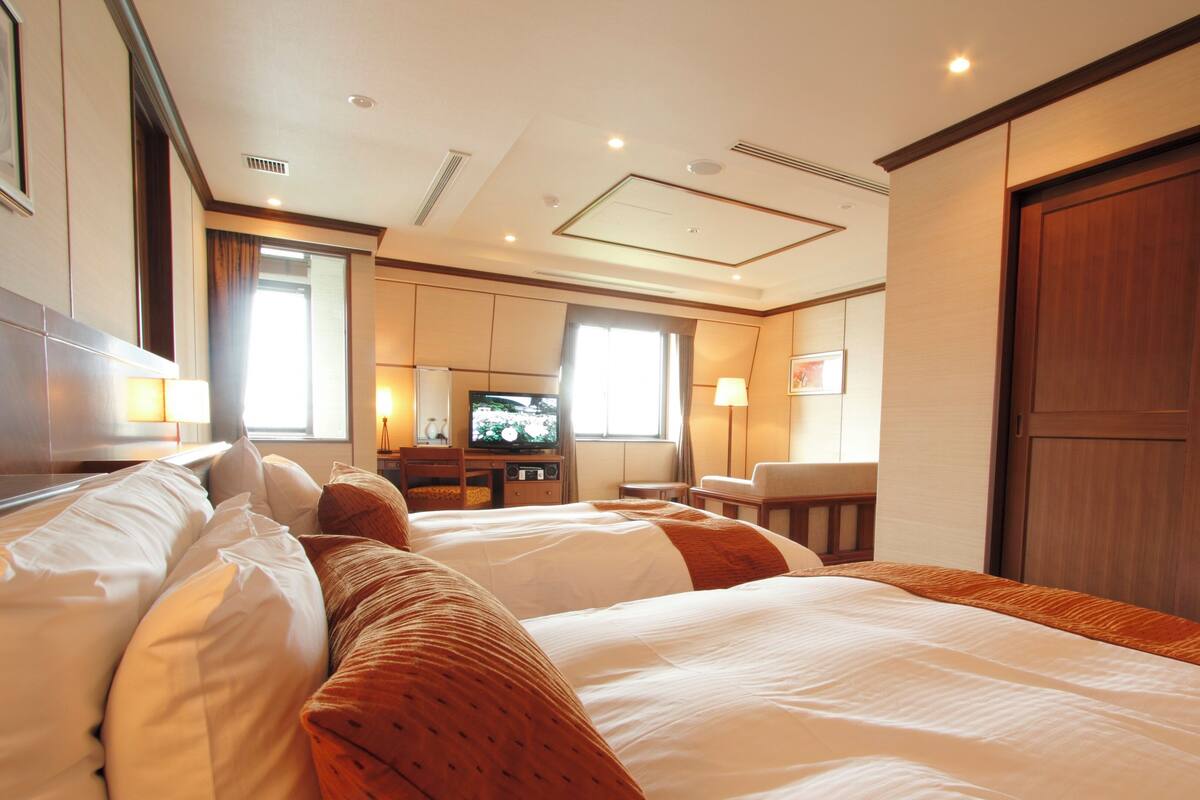 A hotel room with two beds, a television, a desk, and a large wardrobe.