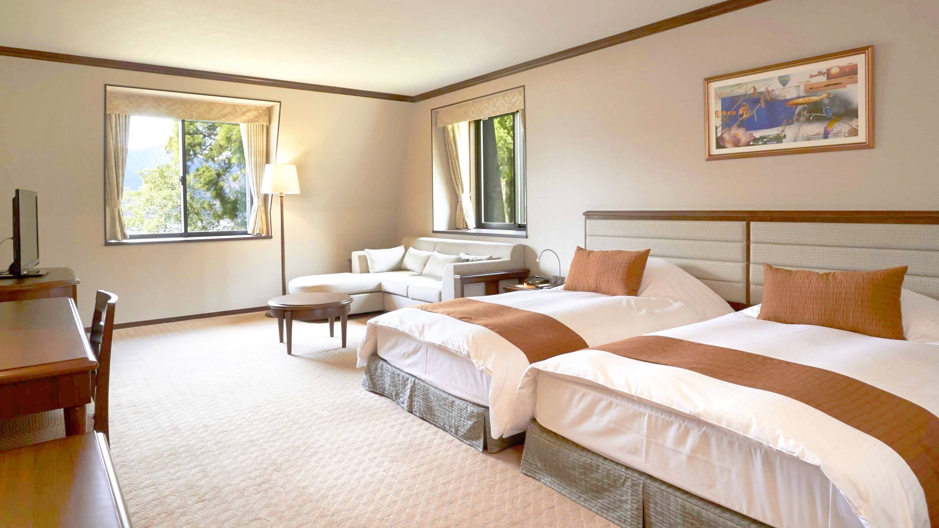 A hotel room with two beds, a sofa, a desk, and a lamp.
